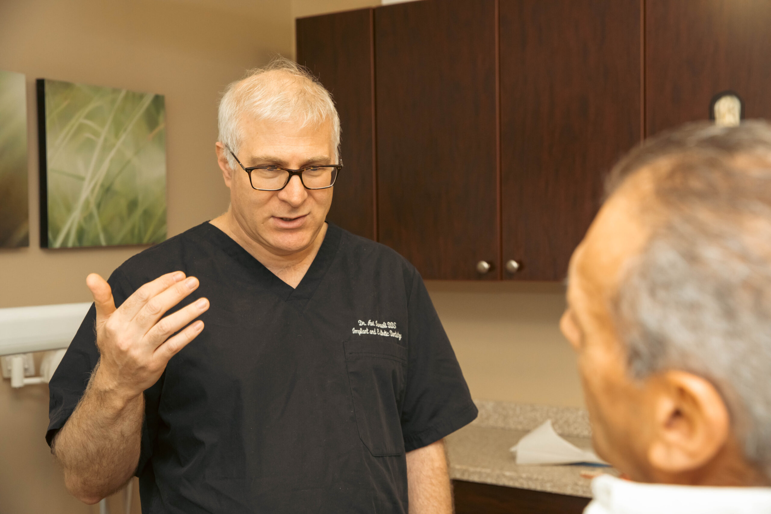 Dr. Isreali talking to a patient, while gesturing with his hands, about his zirconia fixed bridge procedure.